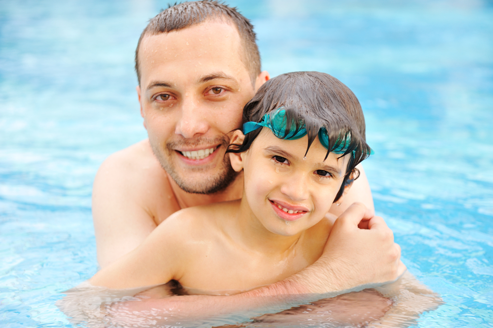 Smiling father and son leaning in the water pool